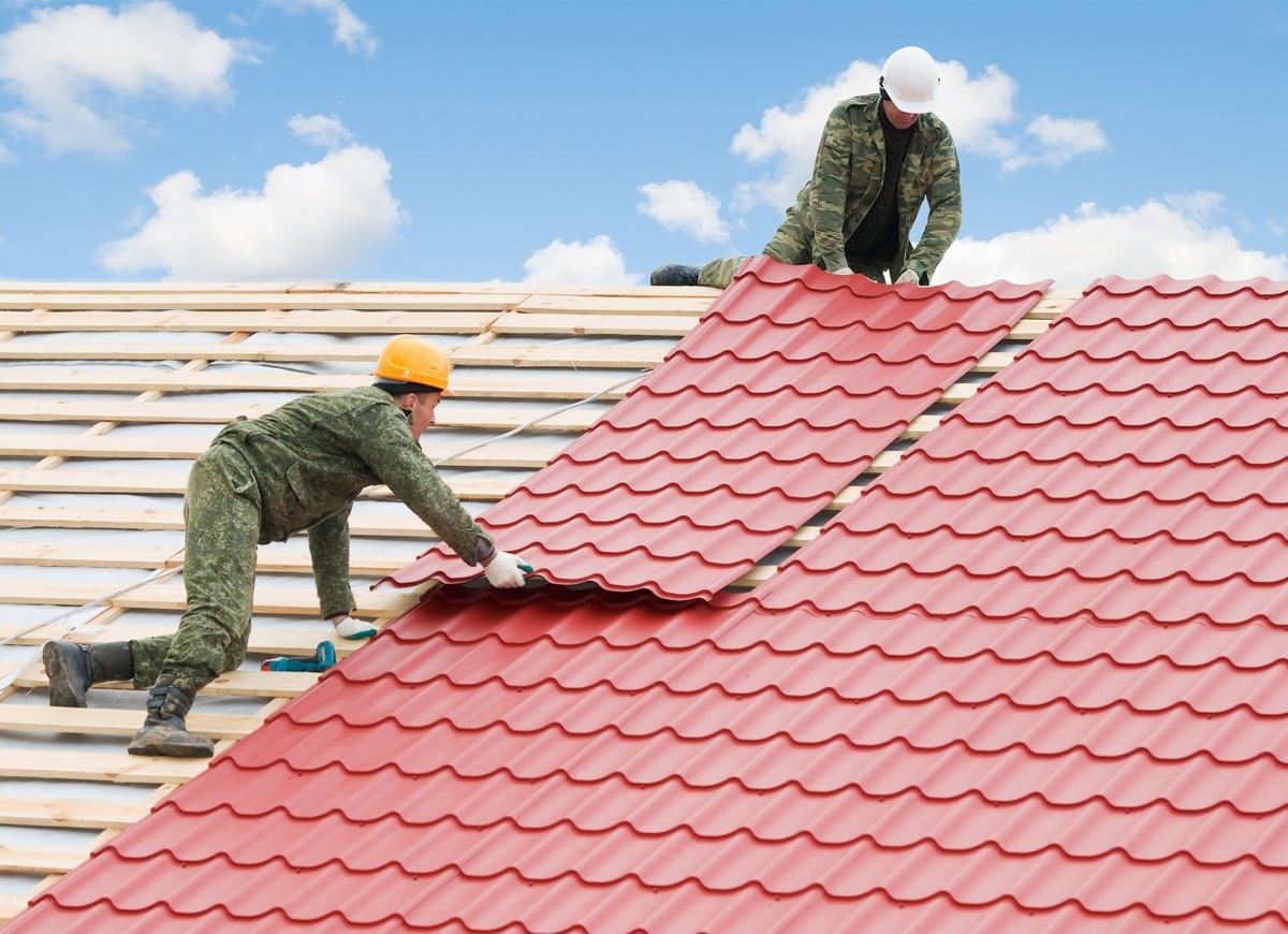 Two workers on roof at works with metal tile and roofing iron