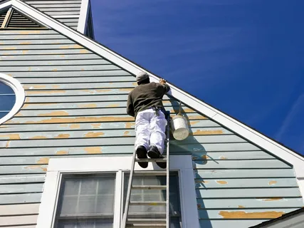 Professional painters applying fresh paint to the exterior walls of a residential home, using high-quality tools and materials for a flawless finish.